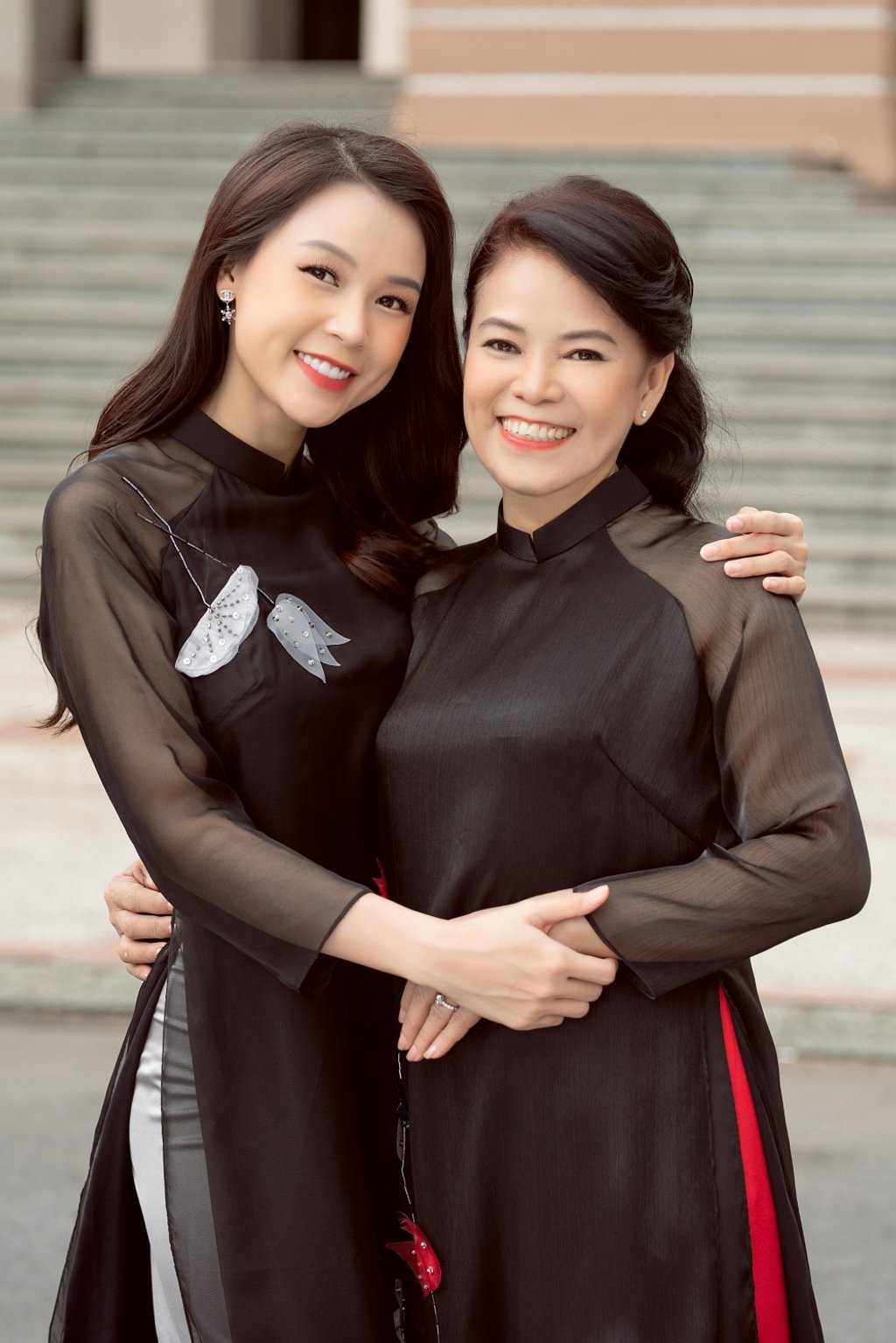 Bộ áo dài mang gam màu đen được tô điểm hoa văn hoa sen dịu dàng bằng thanh ngọc khiết càng giúp hình ảnh của hai mẹ con thêm phần duyên dáng, ngọt ngào.